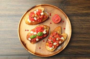 Domatesli lezzetli bruschettalar, mozzarella peyniri ve fesleğen ahşap masada servis edilir.