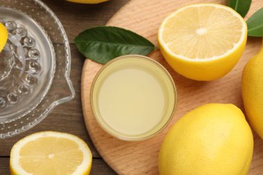 Bardakta limon suyu, yapraklar, meyve sıkacağı ve ahşap masada taze limon.