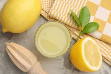 Bardakta limon suyu, sıkma, yapraklar ve açık gri masada taze limonlar.