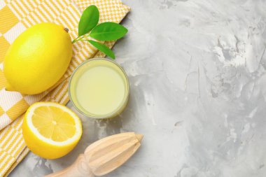 Bardakta limon suyu, sıkma, yapraklar ve açık gri masada taze limonlar. Metin için boşluk