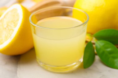 Bardakta limon suyu, yapraklar ve açık gri masada taze limonlar, yakın plan.