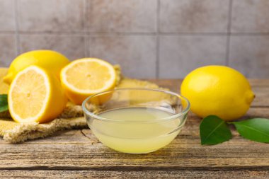 Tabakta limon suyu, yapraklar ve ahşap masada taze limonlar, yakın plan.