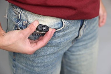 Cebinde gizli kamera olan genç bir kadın açık gri arka planda, yakın plan.