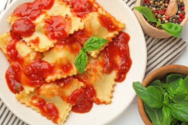 Beyaz ahşap masada domates soslu, fesleğen ve baharatlı lezzetli ravioli.