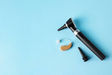 Modern otoskop, işitme cihazı ve açık mavi arka planda kulak spekulumları, düz yatış. Metin için boşluk