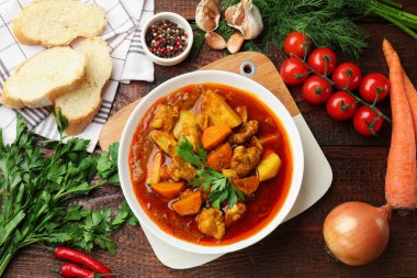 Lezzetli pişirilmiş güveç taze malzemeler ve ahşap masa üzerinde ekmek, düz yatıyordu.