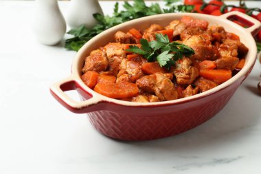 Pişirme kabında nefis pişirilmiş güveç ve beyaz mermer masada taze malzemeler, yakın plan.