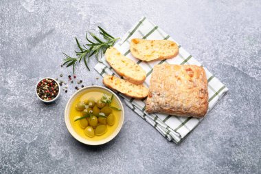 Taze kesilmiş ciabatta, yağ, zeytin, biberiye ve biberiyeler gri desenli masada, düz yatıyordu.