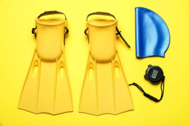 Flippers, dijital kronometre ve sarı arka planda yüzme şapkası, düz yatış