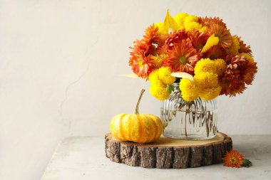 Sonbahar atmosferi. Güzel çiçekli vazo ve açık gri masada balkabağı, metin için boşluk