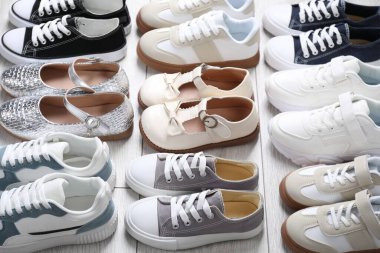 Gri ahşap zeminde birçok şık çocuk ayakkabısı var.