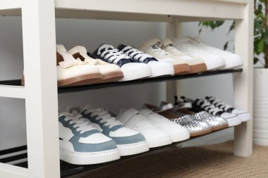 Beyaz duvarın yanındaki depoda farklı çocukların ayakkabıları var.