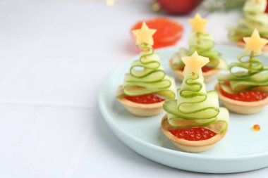 Kırmızı havyar, salatalık, peynir ve beyaz masa üzerindeki şenlikli dekordan yapılmış Noel ağacı şekilli turtalar.