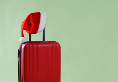 Noel tatili. Zeytin arka planında Noel Baba şapkası olan kırmızı bavul, yakın plan. Metin için boşluk