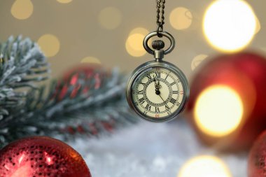 Cep saati, parlak mücevherler, köknar dalları ve bulanık ışıklara karşı yapay kar, yakın plan. Yeni yıl tebrik kartı.