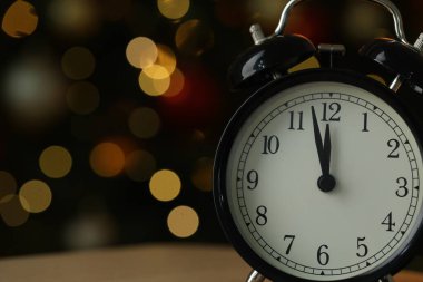 Masanın üzerindeki çalar saat koyu arkaplanda bulanık ışıklar, metin için boşluk ile yakın plan. Yeni yıl tebrik kartı.