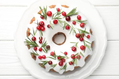 Beyaz ahşap masa üzerinde kremalı, kızılcıklı ve biberiyeli lezzetli bir Noel pastası.