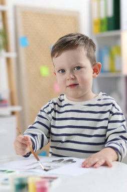 Beyaz masa içinde fırçayla çizim yapan sevimli küçük çocuk.