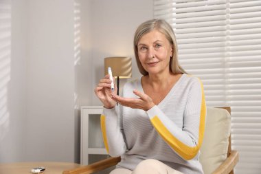 Diyabet. Kan şekeri seviyesini evdeki koltukta tükenmez kalemle ölçen bir kadın. Metin için boşluk