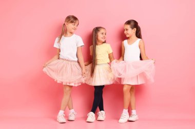 Pembe arka planda poz veren şirin küçük kızlar.
