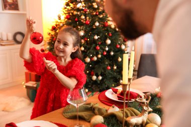 Süslü küçük kız babasıyla evde Noel kutlaması için hazırlanıyor.