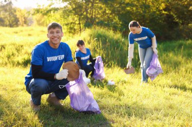 Çantalı bir grup mutlu gönüllü parkta çöp topluyor.