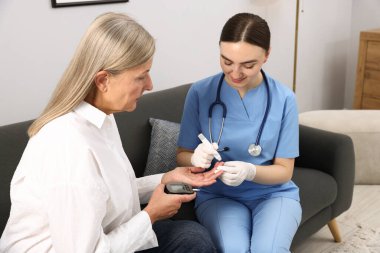 Diyabet. Tıbbi eldivenli gülümseyen doktor evdeki kanepede neşterli kalemle hastanın kan şekerini ölçüyor.