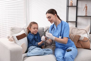 Diyabet. Tıbbi eldivenli gülümseyen doktor, küçük kızın kanındaki şeker seviyesini kapalı koltuktaki tükenmez kalemle ölçüyor.