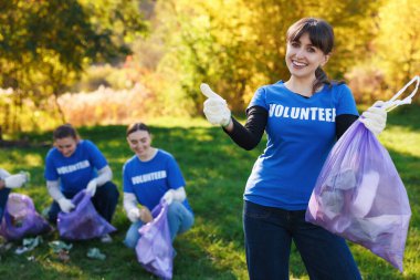 Çantalı bir grup mutlu gönüllü parkta çöp topluyor, seçici odaklı.