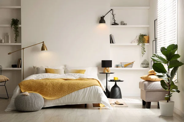 Yatak odasında çarşaflı, komodinli, puf ve raf üniteli büyük bir yatak.