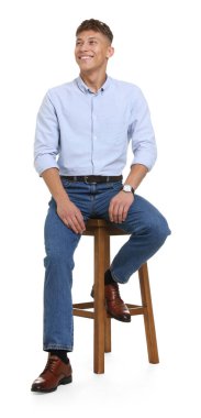 Beyaz arka planda taburede şık kotlar giyen yakışıklı genç adam.