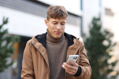 Şehir caddesinde akıllı telefonu olan ceketli yakışıklı bir adam.