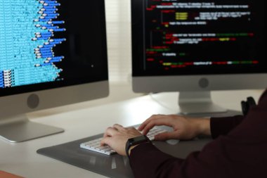 Ofisteki beyaz masada çift monitörlü bilgisayar üzerinde çalışan programcı, yakın plan