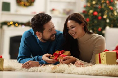 Hediye kutusu olan mutlu çift Noel için dekore edilmiş odada birlikte vakit geçiriyor.