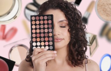 Göz falı paleti olan güzel bir makyaj sanatçısı pembe arka planda yere düşen dekoratif kozmetiklere karşı.