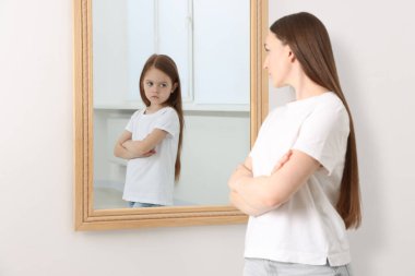 Genç bir kadın kendini aynada küçük bir kız olarak görüyor. Kişilik kavramı, geçmiş ve gelecek, zaman akışı, yaş