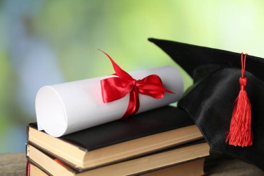Diploma, mezuniyet şapkası ve kitap yığını bulanık arka plan, yakın plan