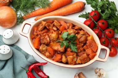 Pişirme kabında nefis pişirilmiş güveç ve beyaz mermer masada taze malzemeler, düz konum