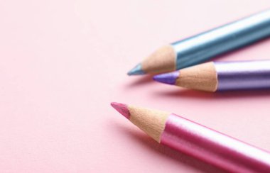 Pembe arka planda parlak göz kalemleri, yakın plan. Metin için boşluk