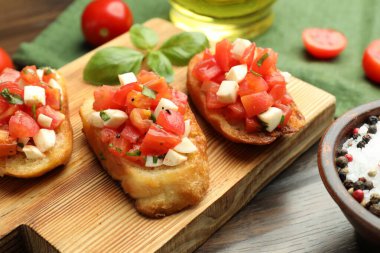 Domatesli lezzetli bruschettalar, mozzarella peyniri ve fesleğen ahşap masada servis edilir, yakın plan.