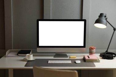 Ofisteki beyaz masa üzerinde beyaz ekran ve gri hasırlı bilgisayar. Şık bir iş yeri