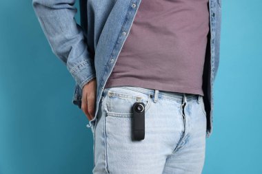 Açık mavi arka planda cebinde gizli casus kamerası olan adam, yakın plan.