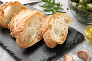 Ciabatta dilimleri, baharatlar ve zeytinler gri masada, yakın plan.