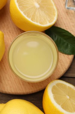 Bardakta limon suyu, yapraklar ve ahşap masada taze limonlar.