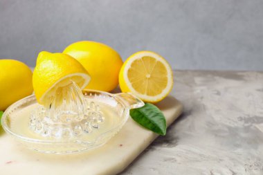 Meyve sıkacağında limon suyu, yapraklar ve açık gri masada taze limonlar, yakın plan. Metin için boşluk