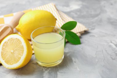Bardakta limon suyu, sıkma, yapraklar ve açık gri masada taze limonlar, yakın plan. Metin için boşluk
