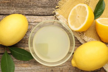 Tabakta limon suyu, yapraklar ve ahşap masada taze limonlar.