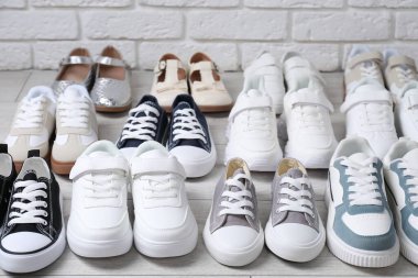 Beyaz tuğla duvarın yanında, gri ahşap zeminde birçok şık çocuk ayakkabısı var.