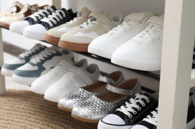 Beyaz duvarın yanındaki depoda farklı çocukların ayakkabıları var.