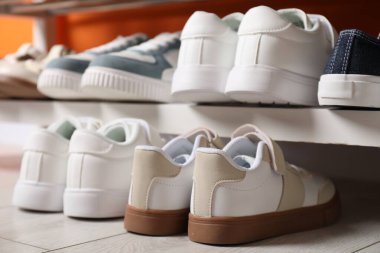 Farklı çocukların ayakkabıları raflarda ve turuncu duvarın yanında, kapalı.